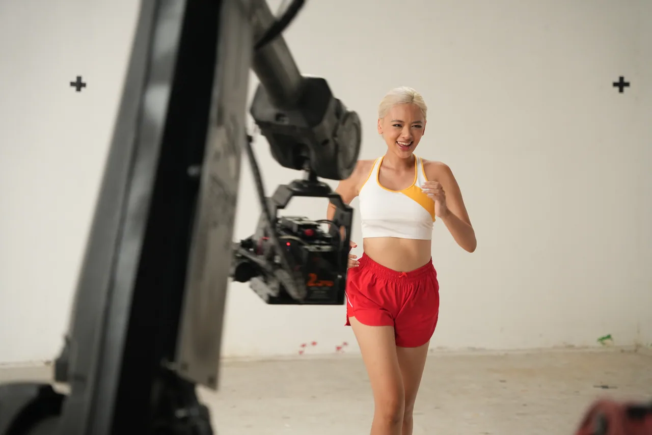 A runner sprinting straight into the lens on the white cyclorama, the arm holding the camera low in the foreground
