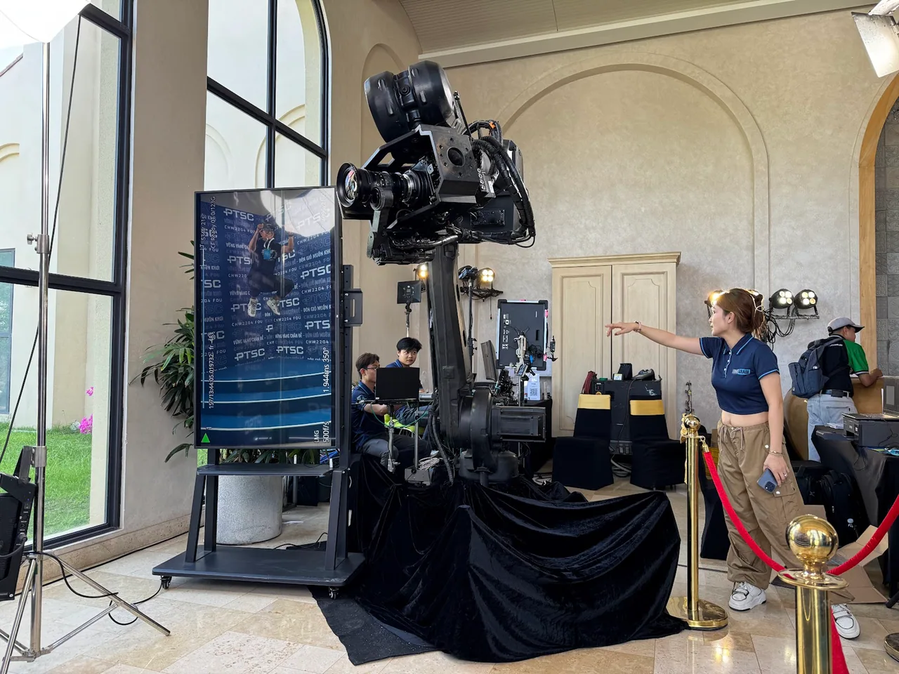 The glambot arm draped in black velvet behind a red rope at an event, a guest’s slow-motion clip playing back on the screen beside it