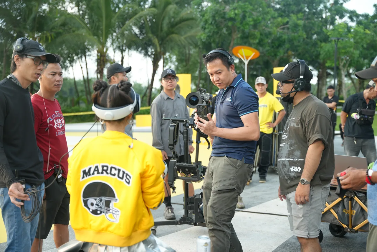 The crew gathered around the camera on a park location, talent waiting in frame
