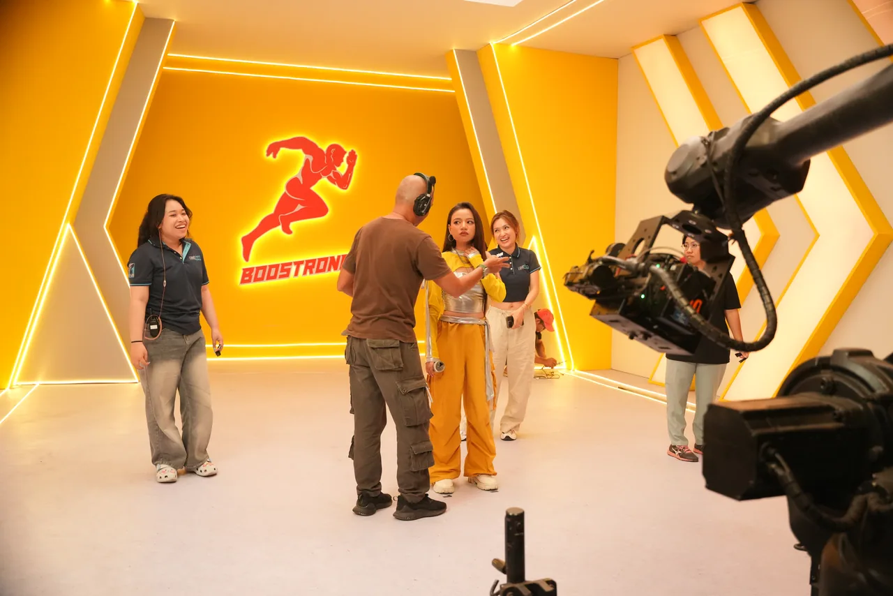 Crew and talent together on a chevron-lit amber commercial set, the camera arm holding at frame right