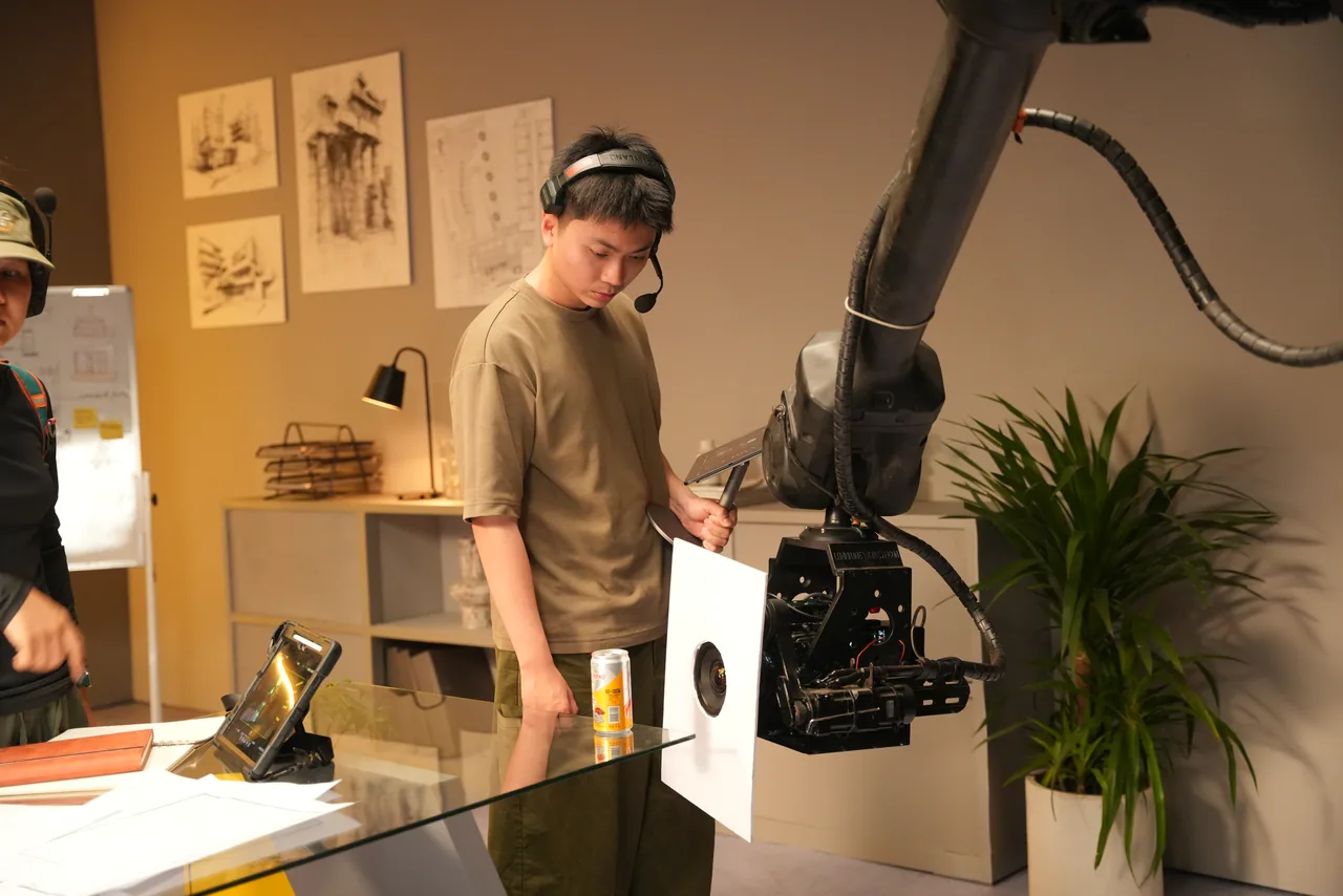 The camera arm dipping over a table-top product set-up while an assistant flags the light